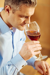 Relaxation. Good-looking concentrated blond man drinking wine and wearing a blue shirt while relaxing