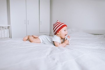 infant child in red and white striped hat with pompom playing with toy deer in bed