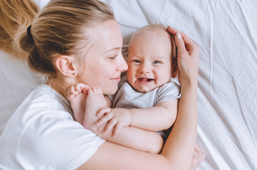 top view of mother cuddling her laughing infant baby in bed