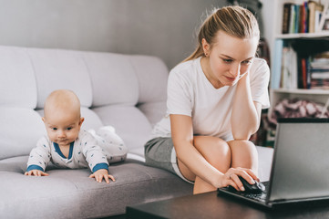 young mother using laptop while little child lying on couch