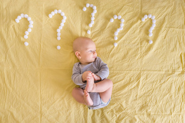 Naklejka premium top view of infant child lying surrounded with question marks made of cotton balls in bed