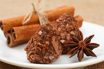 Chocolate candy truffles on white plate with star anise and cinnamon