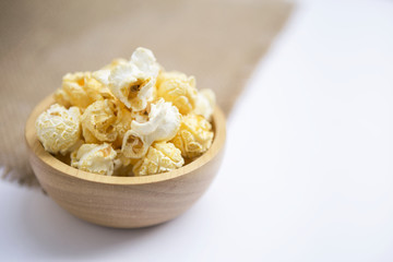 Closeup slated popcorn in round wooden bowl on white background, snack time