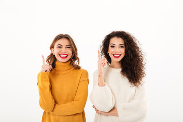 Two smiling girls in sweaters pointing up