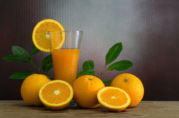 Fresh oranges with green leaf and juice in glass on wooden plate and texture wall background