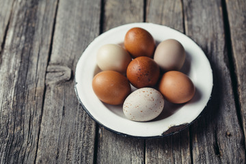 Farm eggs in an old plate on an aged wood planks table, copy space
