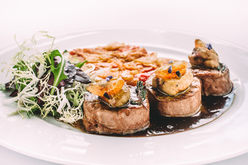 Ragout with meat, mushrooms, dried tomatoes and herbs, on a white round plate. Side view, close-up