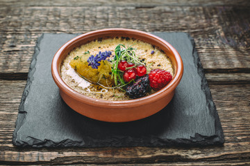 Oatmeal porridge with berries and honey in a clay bowl on a wooden table. Side view