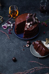 Chocolate layered cake with ganache cream with flowers and biscuit decoration on dark rustic background. Guilty pleasure concept