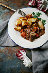 Beef bourguignon in ceramic plate with baked potatoes on metallic background. Rustic concept, natural light.