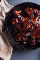 Chicken wings in thick barbecue sauce with garlic on black cast iron pan on gray rustic background.
