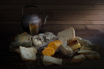 Old Teapot on pile of withered bread and rot on old wooden background and wooden wall which has light splash