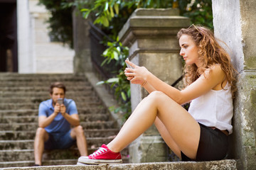 Young couple with smartphones sitting on stairs in town.