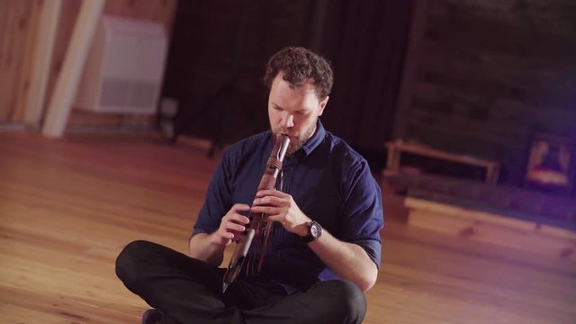 A man sitting on the floor and playing ethnic flute