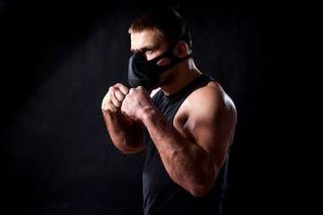 Fototapeta na wymiar A dark-haired male athlete in a black training mask, a sports shirt is boxed against a black isolated background