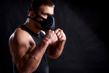 A dark-haired male athlete in a black training mask, a sports shirt is boxed against a black isolated background