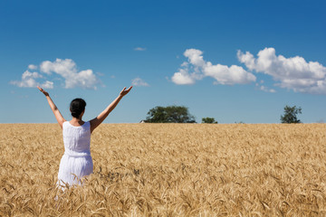 Naklejka na ściany i meble woman in a ripe golden wheat field hugging nature, blue sky with clouds