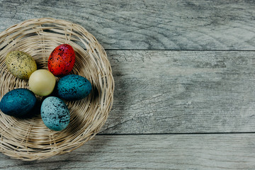 Colorful Dyed Easter Eggs in wicker basket on rustic wooden background aligned to the far left