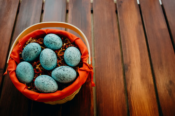 Blue speckled easter eggs in a wicker red lined basket on dark wooden background close up aligned bottom left
