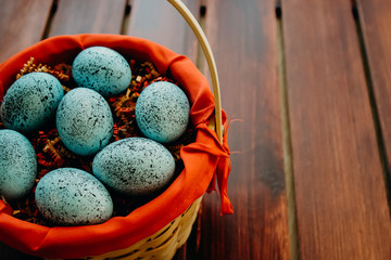 Blue speckled easter eggs in a wicker red lined basket on dark wooden background close up aligned left