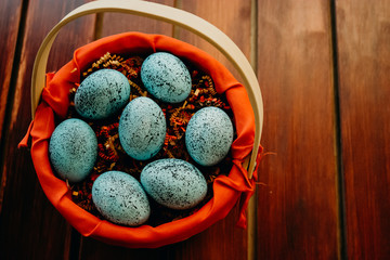 Blue speckled easter eggs in a wicker red lined basket on dark wooden background close up aligned center