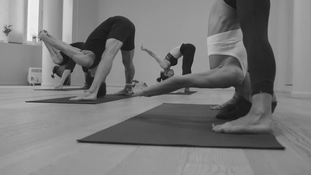 Yoga class. People practicing yoga in bright studio. Ashtanga yoga. Prasarita padottanasana - wide-legged forward bend. Black and white version