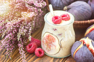 Beautiful healthy appetizer figs fruit smoothie milk shake in glass jar decorated fresh figs pink raspberries  top view. Natural detox Liquid ice cream. Yogurt cocktail dessert wooden background.