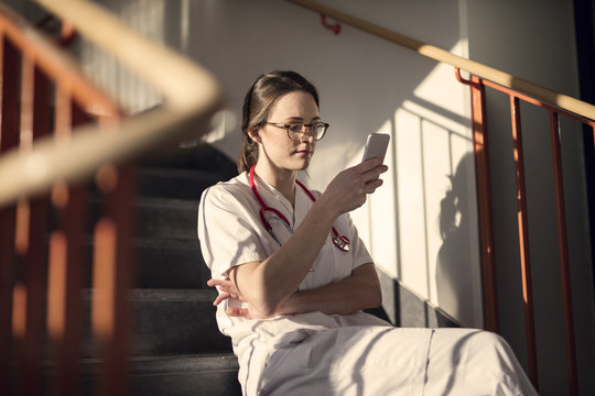 Doctor sitting on stairs with smartphone