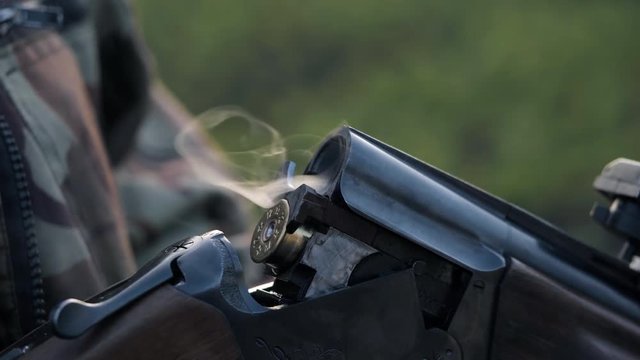Smoke from the trunks of smooth-bore hunting rifle after firing. Hunter in camouflage takes out cartridges from a gun. 4k