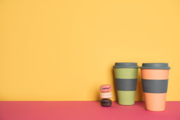 Cup of coffee to go with macaron on yellow and pink background
