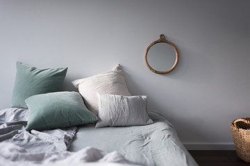 Bett mit Kissen und Spiegel in Pastelltönen im Sonnenschein