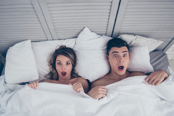 What we did last night? Top view of funny man and woman lying in bed covered by sheets with wide...