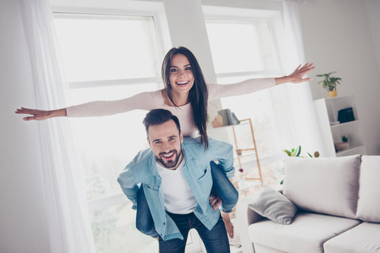 I want to fly higher! Concept of happiness tenderness romantic. Cheerful glad excited cute extremely happy attractive woman is showing a plane riding on her delightful boyfriend's back in a new house