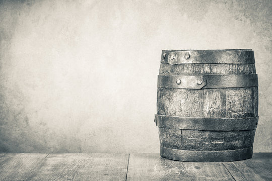 Classic old retro aged oak barrel with hoops on wooden floor front concrete wall background. Vintage style sepia photo