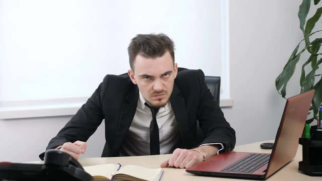 Young angry businessman in suit is sitting in office and showing No by shaking head, gesture 60 fps