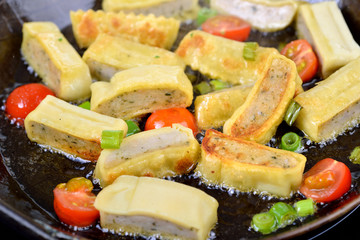 Geschnittene schwäbische Maultaschen mit Cherrytomaten und Frühlingszwiebeln  beim  Anbraten in heißem Fett - Cut Swabian meat ravioli with cherry tomatoes and spring onions during frying in hot fat