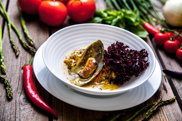 Mussel cooking with lemon and herbs in clay pot over wood background