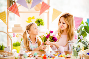 Obraz na płótnie Canvas Charming smiling daughter presenting bouquet of colorful tulips to her pretty mother, together enjoying, celebrating Easter, festive atmosphere at home