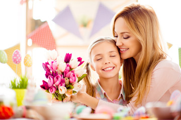 Obraz na płótnie Canvas Attractive, charming, pretty, cute, sweet, lovely mother and daugther celebrating Easter, holding bouquet of colorful tulips, enjoying hugging with each other having eyes closed