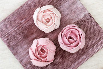 Pink marshmallows flowers roses on old wood plank. Beautifully decorated dessert. Low-calorie sweetness. Top view.