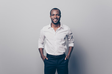 Portrait of glad confident intelligent attractive african man wearing white shirt with rolled-up sleeves holding hands in pockets isolated on gray background - Powered by Adobe