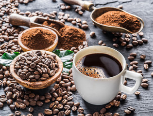 Roasted coffee beans, ground coffee and cup of coffee on wooden table.