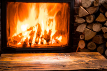 Old wooden table and fireplace with warm fire at the background.