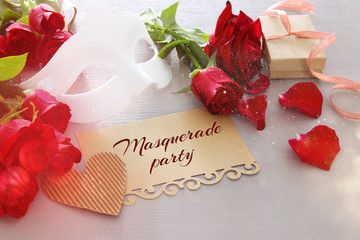 Image of elegant venetian mask and red roses on wooden table