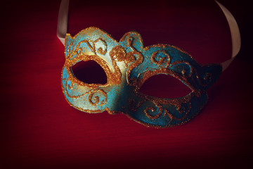 Image of elegant blue and gold venetian mask over red background.