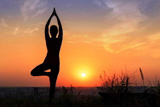 girl does yoga standing tree pose at sunset