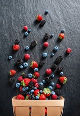 Explosion of different berries. Photo of strawberry, blueberry, blackberry, raspberry in basket on black slate. Top view. High resolution product.