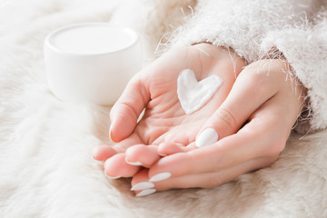 Beautiful groomed woman's hands with cream jar on the fluffy blanket. Moisturizing cream for clean and soft skin in winter time. Heart shape created from cream. Love a body. Healthcare concept. - obrazy, fototapety, plakaty