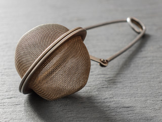 Round metal tea strainer for brewing tea on a black background