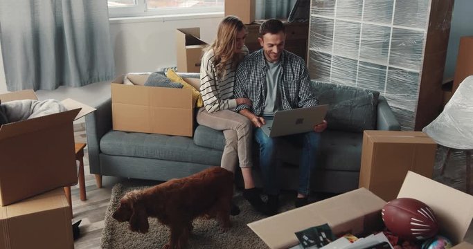 Young nice Caucasian family moving to new apartment with modern design. Husband, wife and dog Spaniel sitting in living room. Indoor.